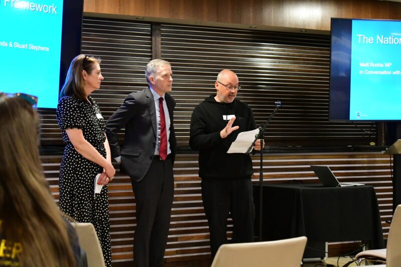 Photograph of three people standing, facing an audience. From left, Amanda Stephens, Matt Rodda and Stuart Stephens.