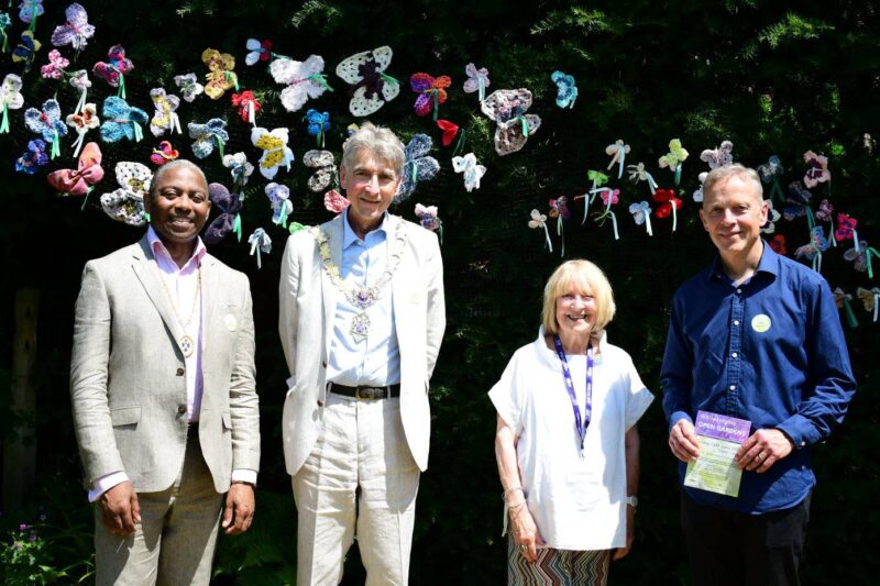 Group featuring Matt Rodda and Mayor of Reading, Tony Page, standing in front of a large coniferous hedge, paper butterflies are embedded in the branches of the hedge.