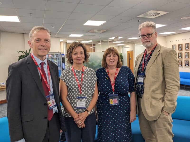 Group photograph set inside an office. From left: Matt Rodda, Professor Julia Waters (Sister of Ruth Perry), Lisa Telling (Chair of Reading Primary Heads), and Edmund Barnett-Ward (parent representative from Caversham Primary School).