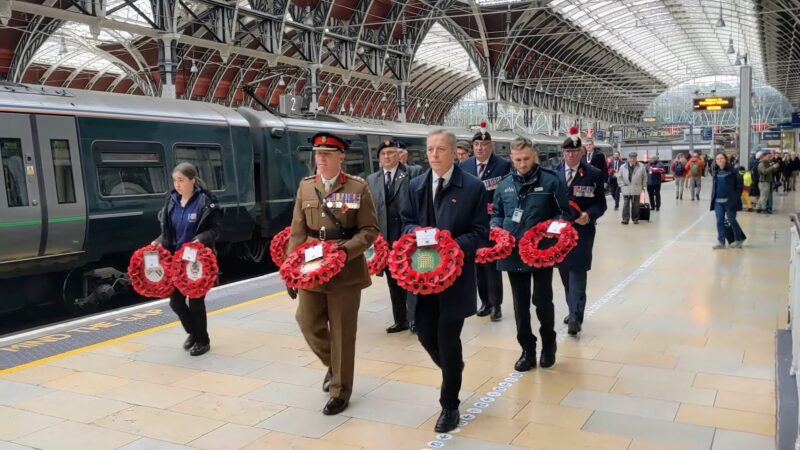 Matt Rodda walking with a group of people inside Paddington Station. They are holding wreaths of poppies.